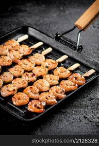 Shrimp on skewers are grilled in a grill pan. On a black background. High quality photo. Shrimp on skewers are grilled in a grill pan.