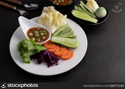 Shrimp-paste sauce in a bowl on the white plate with cucumber, yard long bean, thai eggplant, fried white cabbage, carrots and salad.