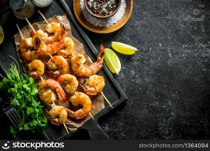 Shrimps on skewers with parsley, spices and lime slices. On dark rustic background. Shrimps on skewers with parsley, spices and lime slices.