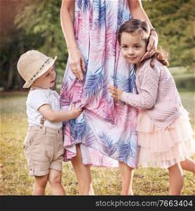 Shy, cheerful chlidren holding embracing the mother’s leg