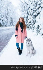 Siberian husky sitting near young woman, snowy forest on background. Cute girl with charming dog. Siberian husky sitting near young woman