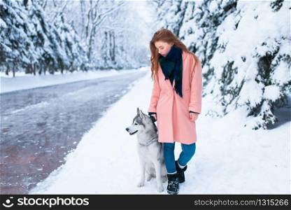 Siberian husky sitting near young woman, snowy forest on background. Cute girl with charming dog