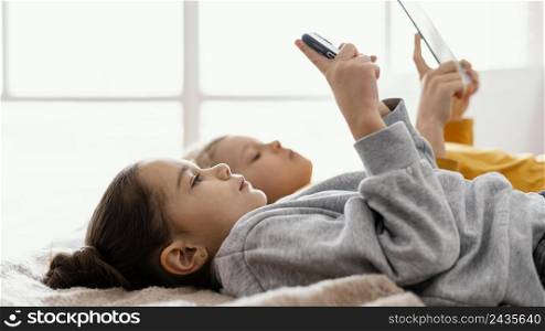 siblings bed playing mobile tablet