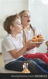 Siblings blowing candles on cupcakes