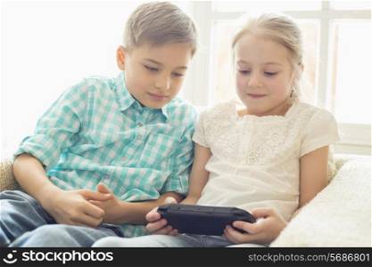 Siblings playing hand-held video game at home