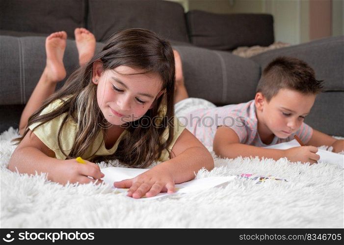 Siblings playing together at home. little boy and girl lying on the carpet and drawing on white sheets of paper with colorful crayons. High quality photography.. Siblings playing together at home. little boy and girl lying on the carpet and drawing on white sheets of paper with colorful crayons