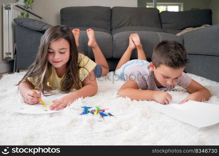 Siblings playing together at home. little boy and girl lying on the carpet and drawing on white sheets of paper with colorful crayons. High quality photography.. Siblings playing together at home. little boy and girl lying on the carpet and drawing on white sheets of paper with colorful crayons