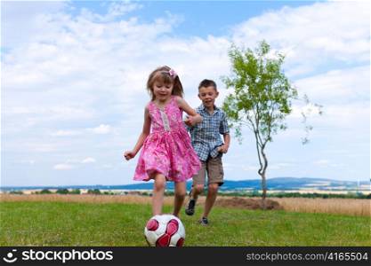Siblings - son and daughter - playing soccer in the garden
