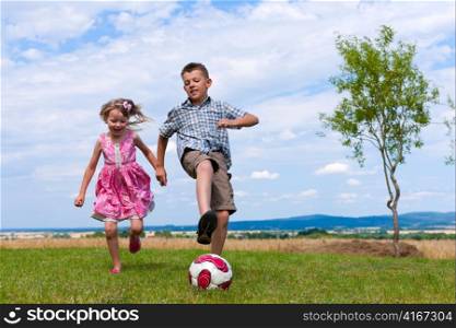 Siblings - son and daughter - playing soccer in the garden