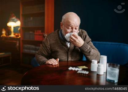 Sick elderly man blows his nose in a handkerchief in home office, age-related diseases. Mature senior is ill and being treated in his house. Sick elderly man blows his nose in home office