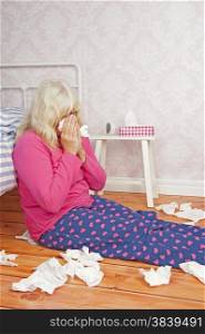 Sick female with pink pajama and tissues sitting on floor next to bed