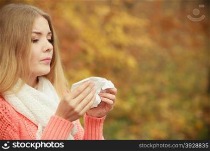 Sick ill woman in autumn park sneezing in tissue.. Sick woman in fall autumn park sneezing in tissue. Ill girl caught cold flu outdoor. Rhinitis or allergy. Health care.