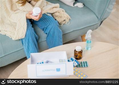 Sick ill young woman cold she covered blanket hold pills bottle read medicine prescription label, female checking ingredient information on sofa at house, pharmacy health care medicament concept