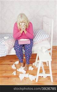Sick lady with pink pajama and tissues sitting on bed blowing her nose