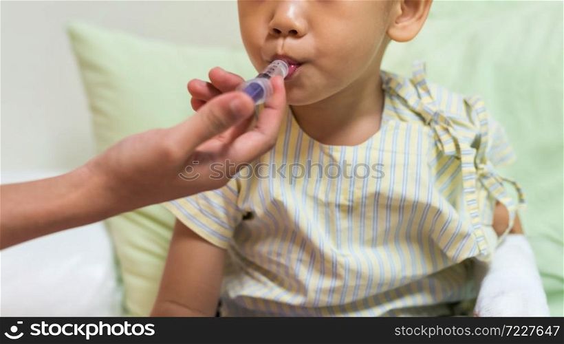 Sick little boy take liquid medicine on syringe by nurse hand on hospital bed. Kid insurance and health care concept. child with IV drip needle piercing with copy space for text. RSV, covid-19.