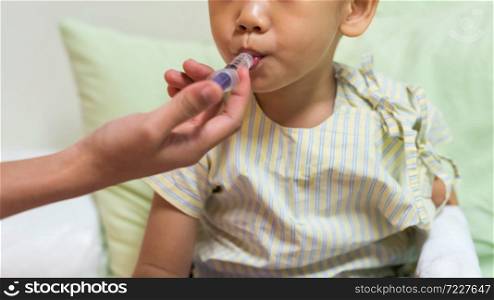 Sick little boy take liquid medicine on syringe by nurse hand on hospital bed. Kid insurance and health care concept. child with IV drip needle piercing with copy space for text. RSV, covid-19.