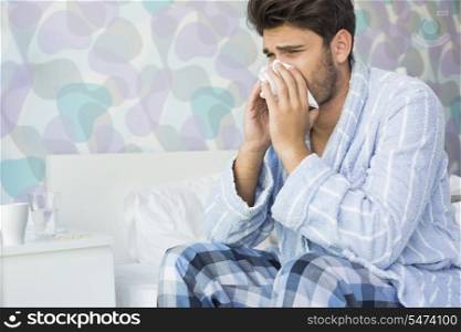 Sick man blowing his nose in tissue paper on bed at home