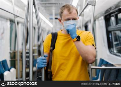 Sick man coughs, wears medical mask and protective rubber gloves, commutes to work in metro carriage, poses in public transport. Spread of coronavirus, influenza, transportation, epidemic concept
