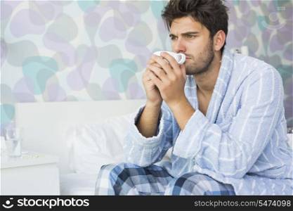 Sick man drinking coffee while sitting on bed at home