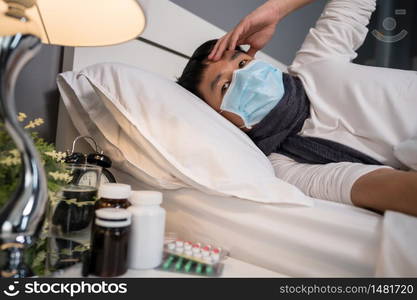 sick man in medical mask is headache and suffering from virus disease and fever in a bed, coronavirus (covid-19) pandemic concept.