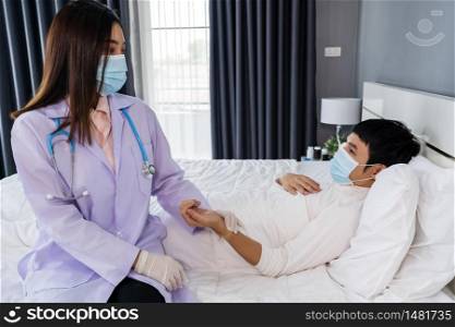sick man lying in a bed while doctor checking his pulse, people must be wearing medical mask protecting from coronavirus(covid-19) pandemic