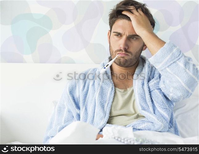 Sick man with thermometer in mouth sitting on bed at home