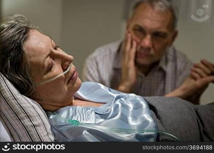Sick mature woman lying in bed worried husband holding hands