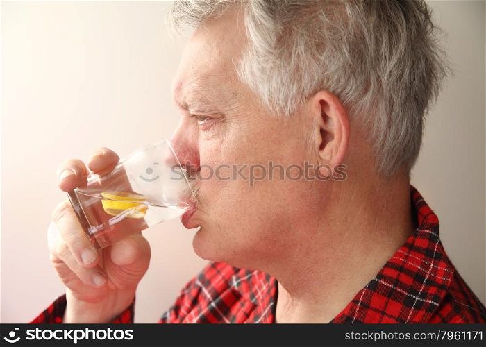 sick senior man in pajamas drinking water with lemon slices
