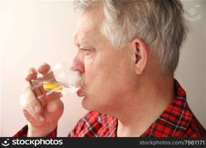 sick senior man in pajamas drinking water with lemon slices