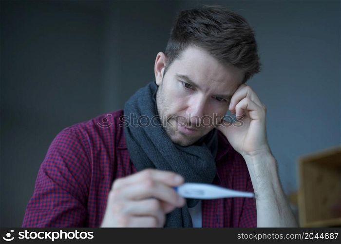 Sick unhealthy German man office worker looking at thermometer, suffer of flu influenza while sitting at his workplace, Ill male employee measuring body temperature at work. Sick unhealthy German man office worker looking at thermometer, suffer of flu influenza