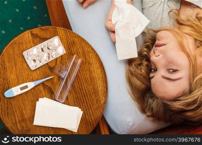 Sick woman in bed. Pills and thermometer on table.. Sick woman laying in bed under wool blanket. Ill girl caught cold flu. Pills tablets and thermometer on table.