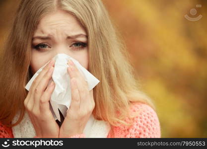 Sick woman in fall autumn park sneezing in tissue. Ill girl caught cold flu outdoor. Rhinitis or allergy. Health care.