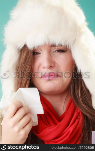 Sick woman in fur hat sneezing in tissue. Ill girl caught winter cold flu in studio on green.