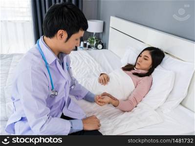 sick woman lying in a bed while doctor checking her pulse