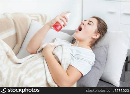 Sick woman lying in living room and using throat spray