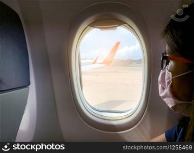 Sick woman wear face mask sit on passenger economy seat near cabin window in airplane. Passenger in departure flight plane at the airport. Novel coronavirus (2019-nCoV) infection or Wuhan coronavirus