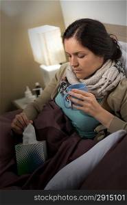 Sick woman with cold flu in bed holding tissue and tea