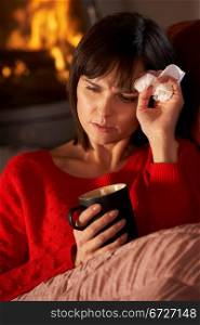 Sick Woman With Cold Resting On Sofa By Cosy Log Fire