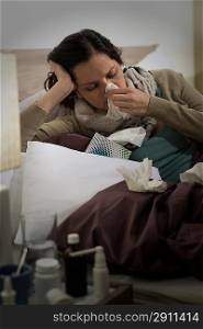 Sick woman with flu sneezing blowing her nose in bed