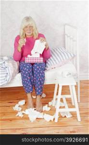 Sick woman with pink pajama and tissues sitting on bed