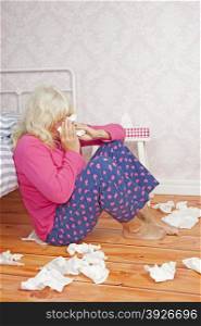 Sick woman with pink pajama and tissues sitting on floor against bed
