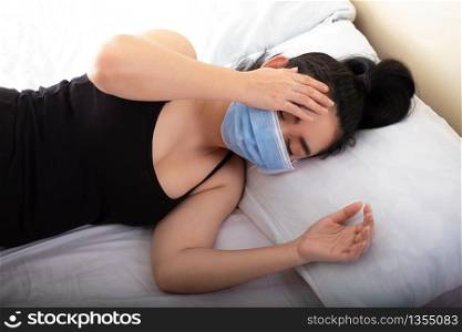 Sick young woman putting medical mask resting sleeping on the bed in the bedroom