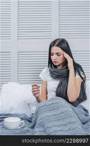 sick young woman sitting bed looking thermometer