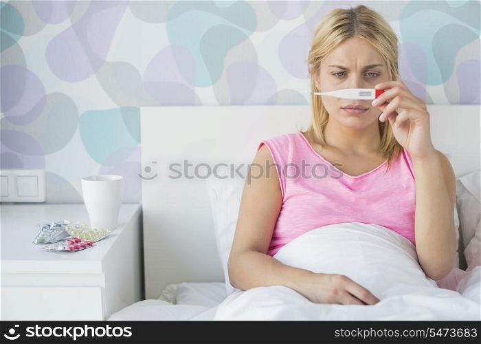 Sick young woman taking temperature with thermometer in bed