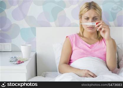 Sick young woman taking temperature with thermometer in bed