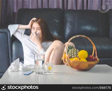 sickness and gynecology concept from woman with allergy, feeling dizzy, sneeze and fever sit at sofa in home, have pills and glass of water laying the table.