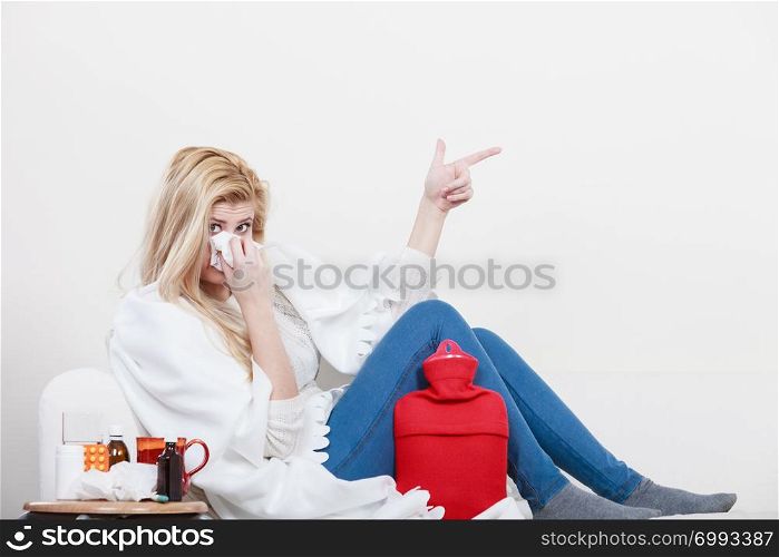 Sickness, seasonal virus problem concept. Woman being sick having flu lying on sofa sneezing into tissue pointing at copyspace. Woman being sick having flu lying on sofa