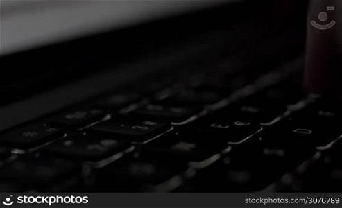 Side Close up male hand typing in dark room with laptop backlit keyboard.