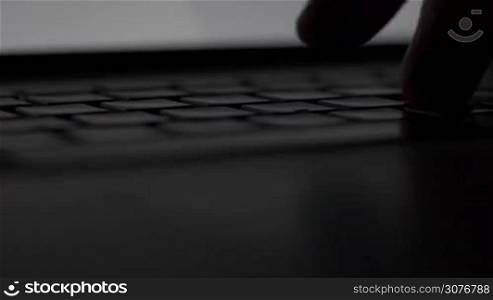 Side macro close up male hand typing in dark room with laptop backlit keyboard.