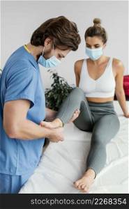 side male osteopathic therapist with medical mask checking female patient s ankle